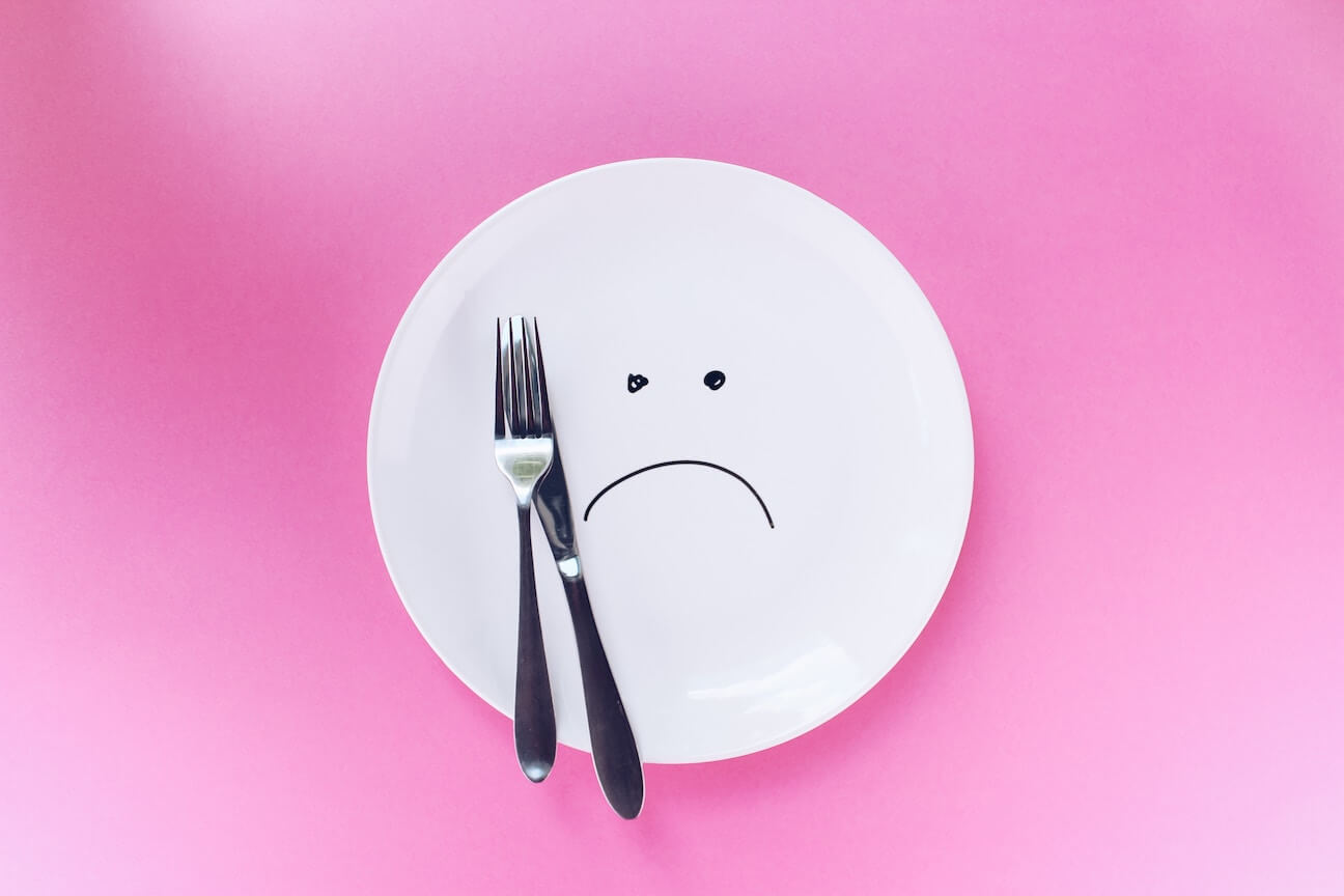 Ein leerer Teller mit einer Zeichnung eines traurigen Smileys: Symbolbild für die Demotivation von Menschen mit Abnehmwunsch, wenn Kalorien zählen nichts bringt.